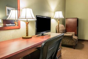 Habitación de hotel con un escritorio de madera, dos lámparas, un televisor, un sillón estampado y un armario.