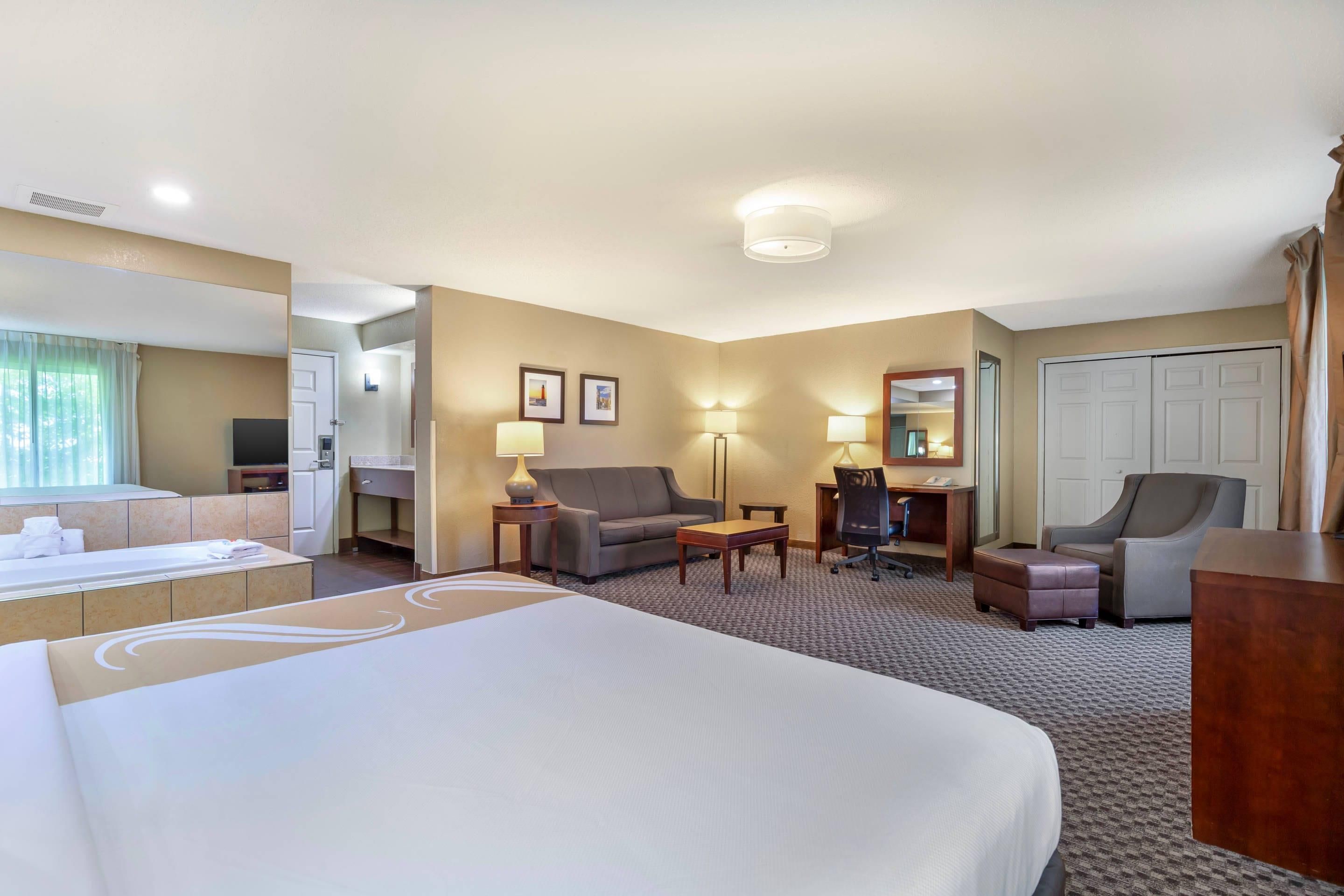 A hotel room with a bed, a desk, a chair, a sofa, and a bathroom.