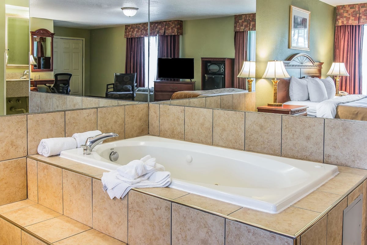A hotel room with a large bathtub, a television, a desk with a chair, and a bed with lamps.