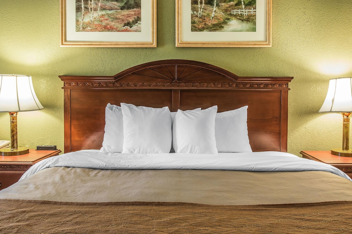 A neatly made bed with a wooden headboard, two bedside lamps, and two framed landscape paintings on the wall.
