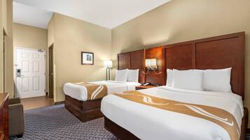 A hotel room with two beds, a desk, a chair, a door, and a framed picture on the wall.