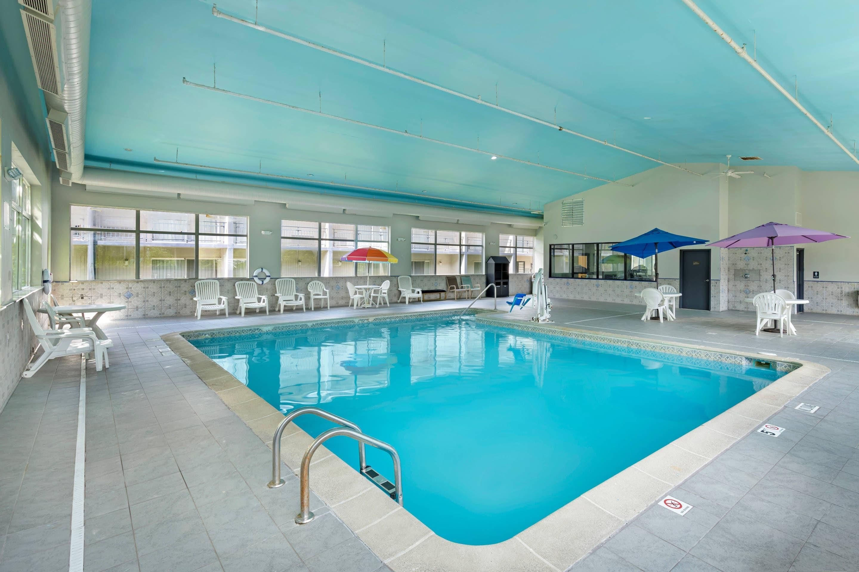 An indoor swimming pool with clear blue water, surrounded by white lounge chairs and umbrellas.