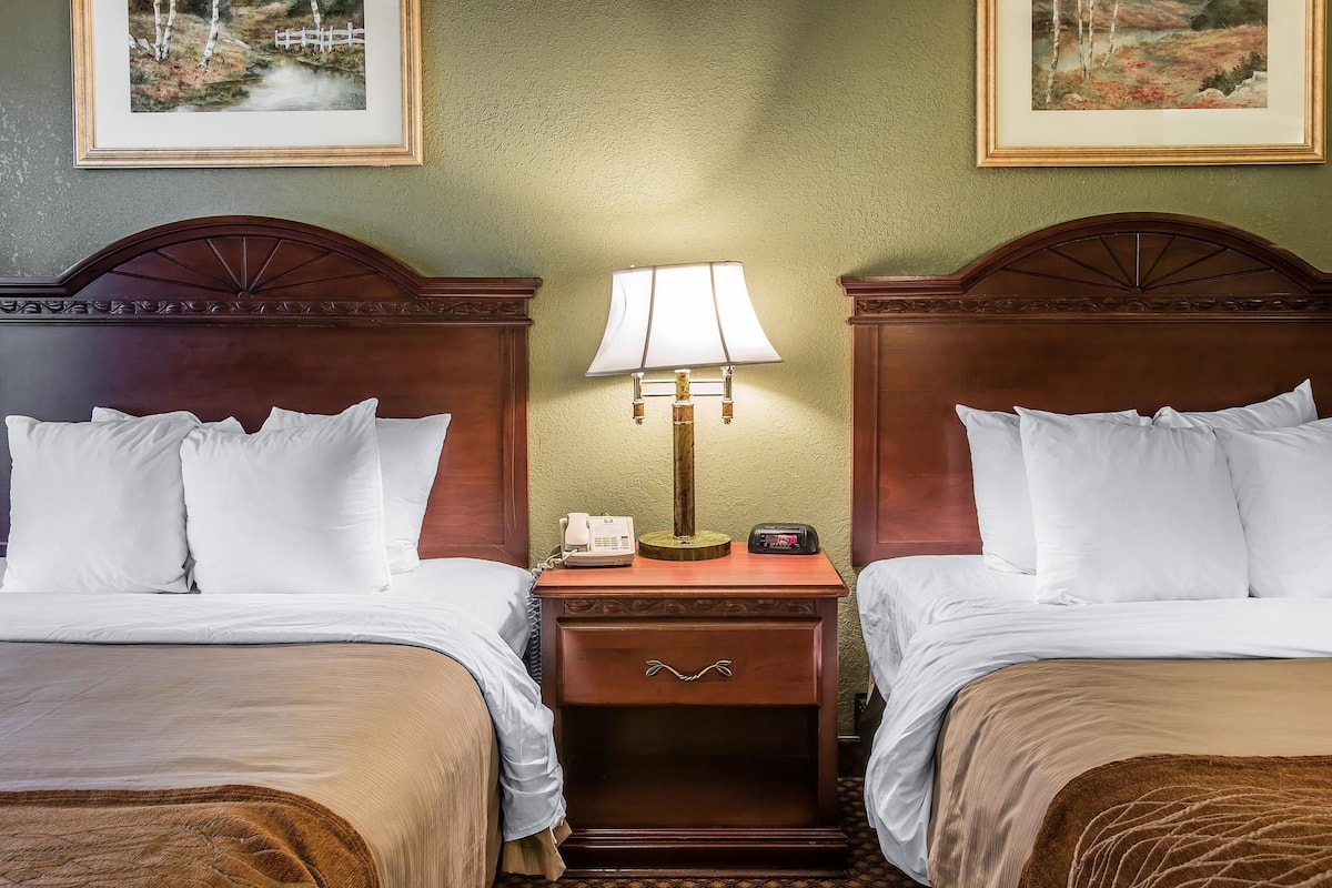A hotel room with two beds, a nightstand with a lamp, a phone, and a drawer.