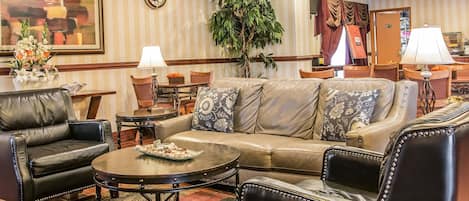 A well-furnished living room with a leather sofa, armchairs, a coffee table, and a large potted plant.