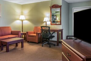 Habitación de hotel con sofá, dos sillones, escritorio, silla, televisor y dos lámparas.
