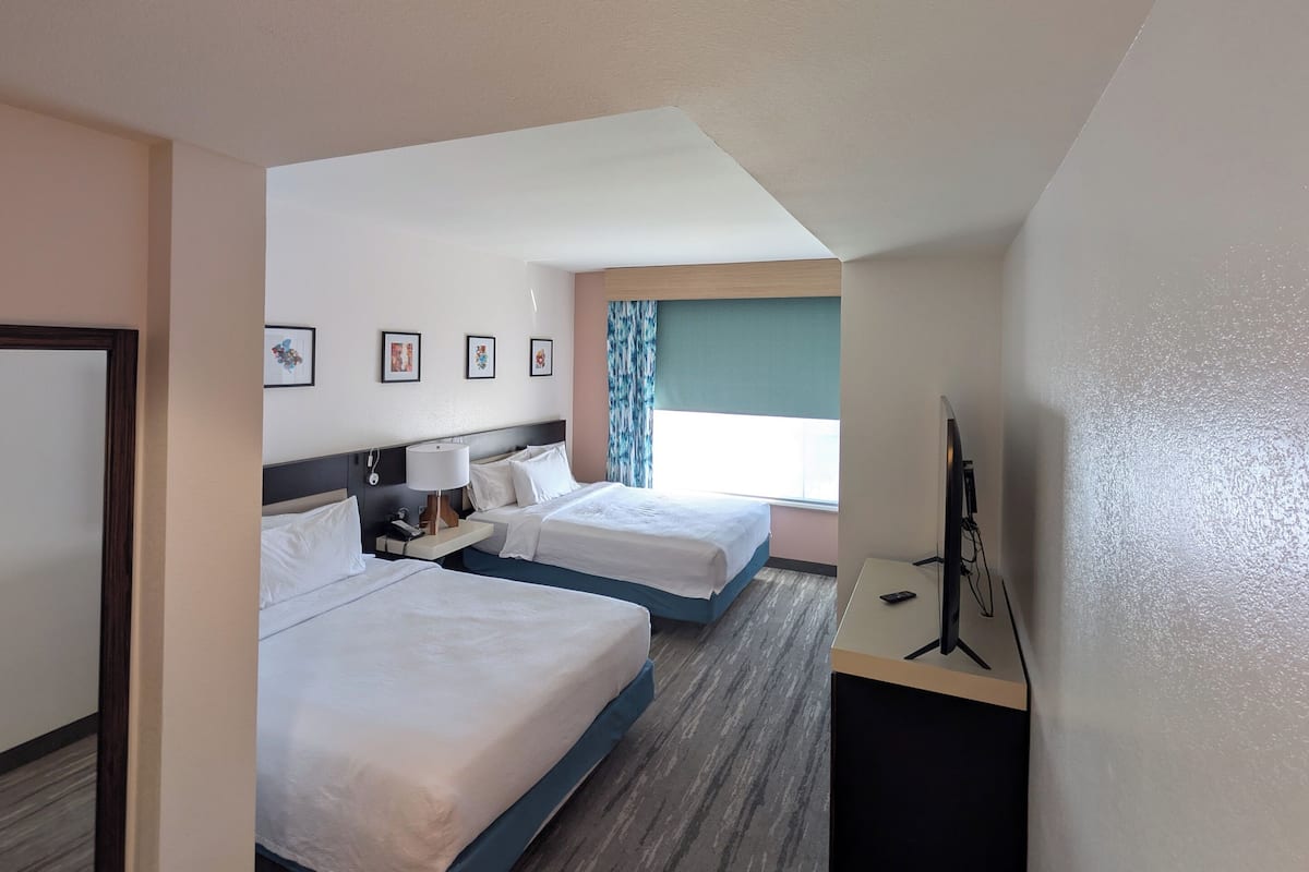 A hotel room with two beds, a desk with a computer, a TV, and framed pictures on the wall.