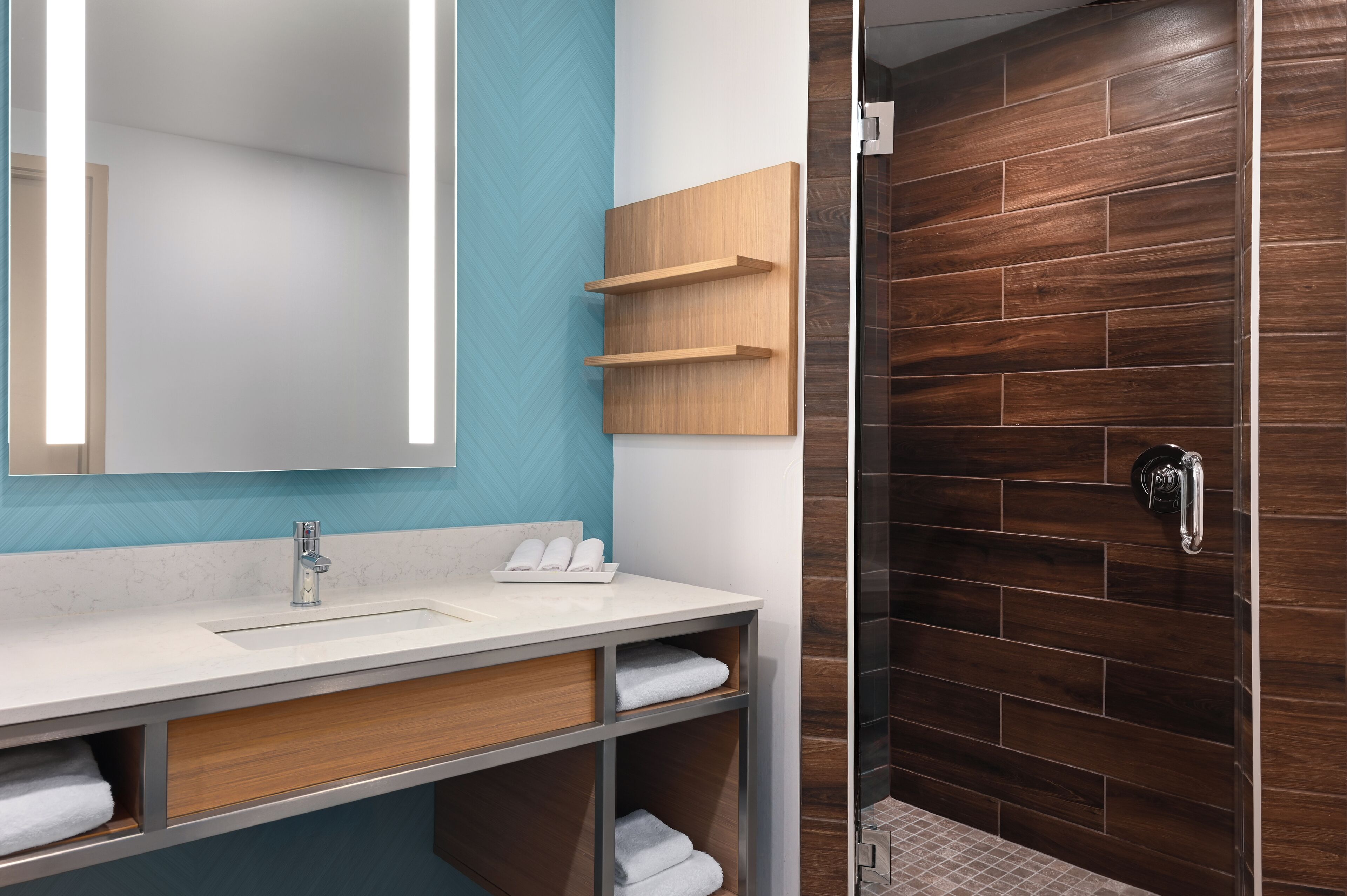 Un bagno moderno con uno specchio grande, un lavandino bianco e un mobile bagno in legno. Sono presenti due portasci da bagno e una doccia con parete in legno.