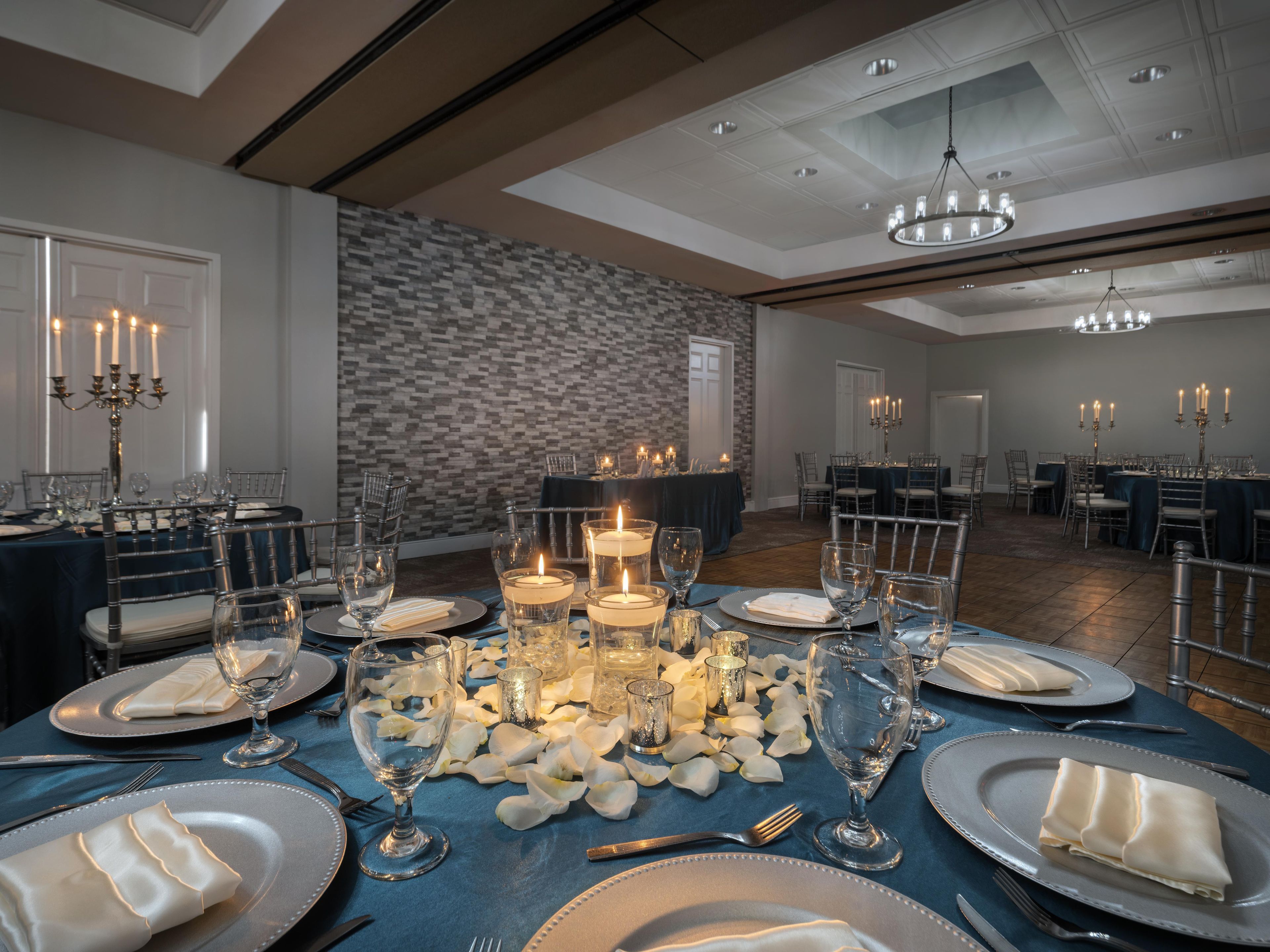 Comedor formal con mesas dispuestas para varios invitados, con velas, cristalería y servilletas dobladas.