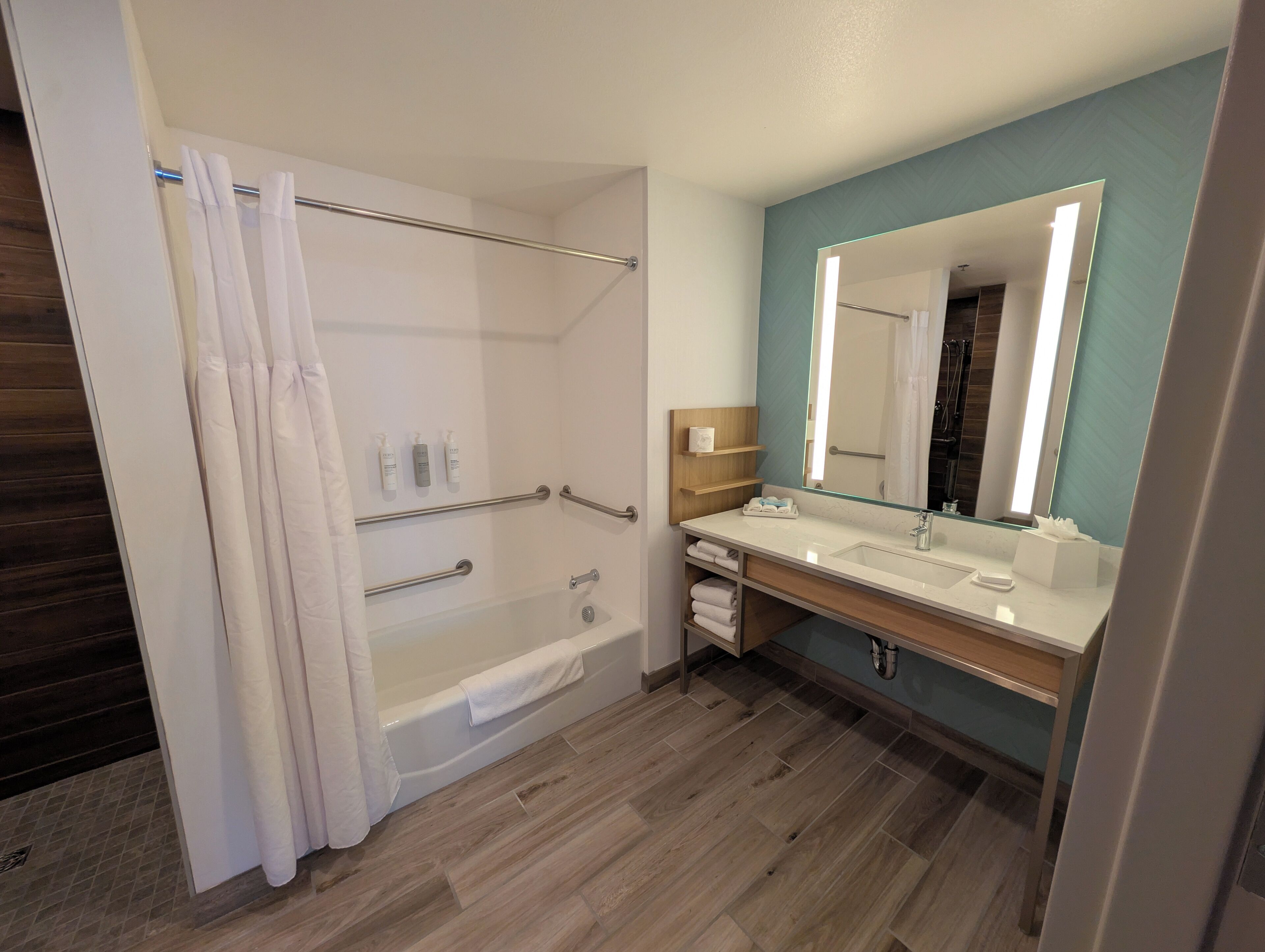 A modern bathroom with a bathtub, a vanity with a mirror, and a shower area with grab bars.