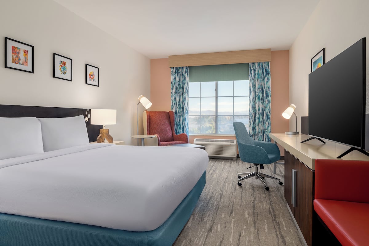 A hotel room with a large bed, a desk, a chair, a TV, and a window with curtains.