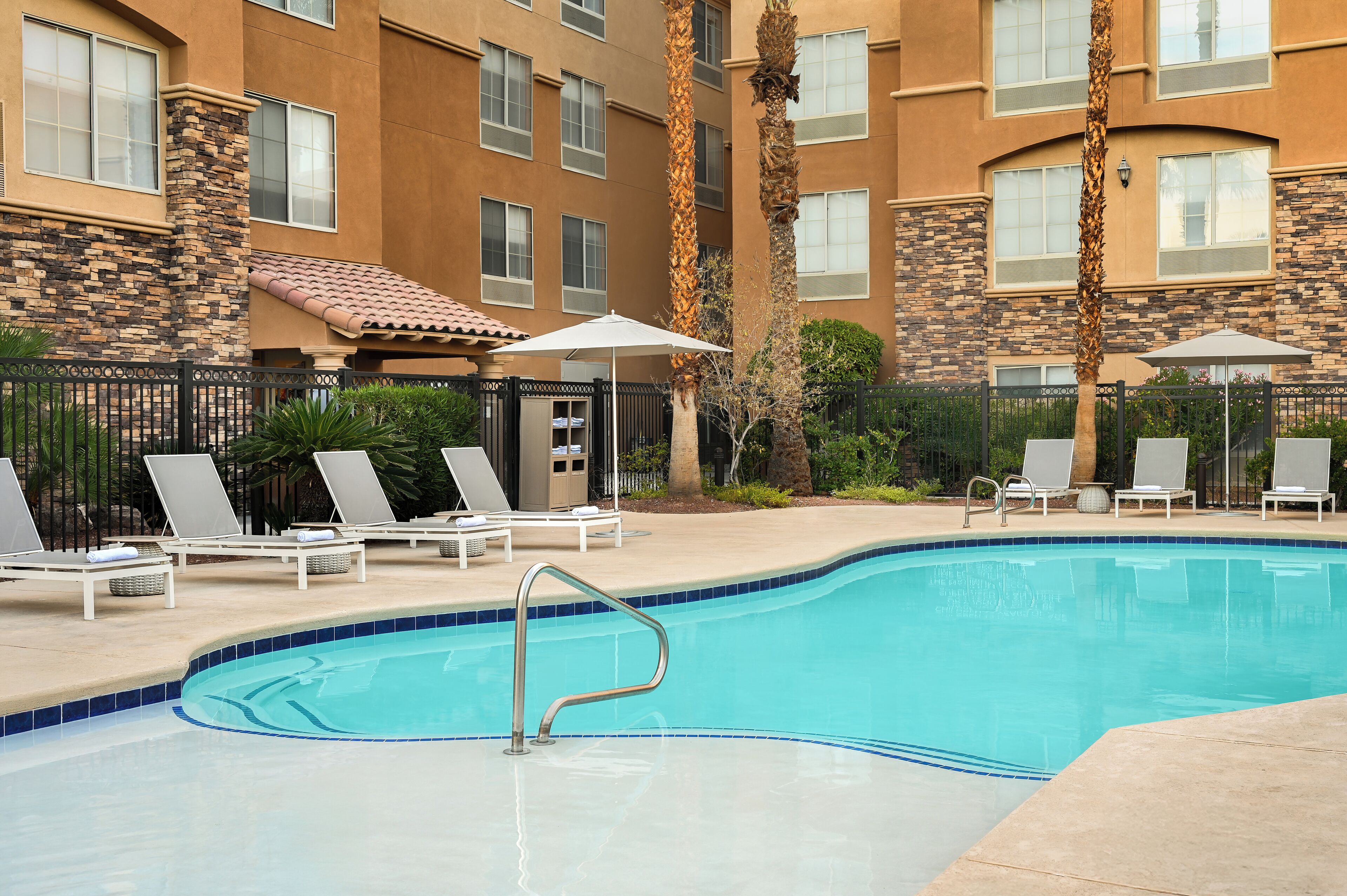 Una piscina al aire libre, sombrillas, sillones reclinables de piscina
