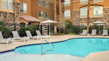 Una piscina al aire libre, sombrillas, sillones reclinables de piscina