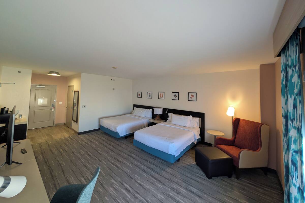 A hotel room with two beds, a desk, a chair, and a small table.