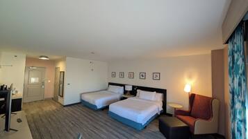 Ein Hotelzimmer mit zwei Betten, einem Schreibtisch, einem Sessel und einem kleinen Tisch.