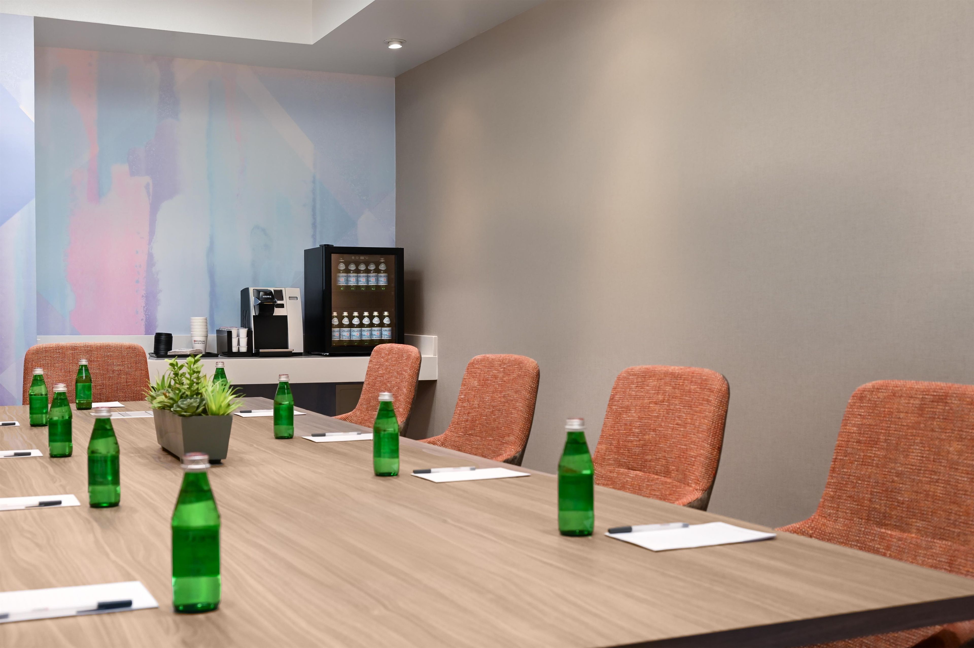 Uma sala de conferência com uma mesa comprida, várias cadeiras, um bebedouro e uma geladeira.