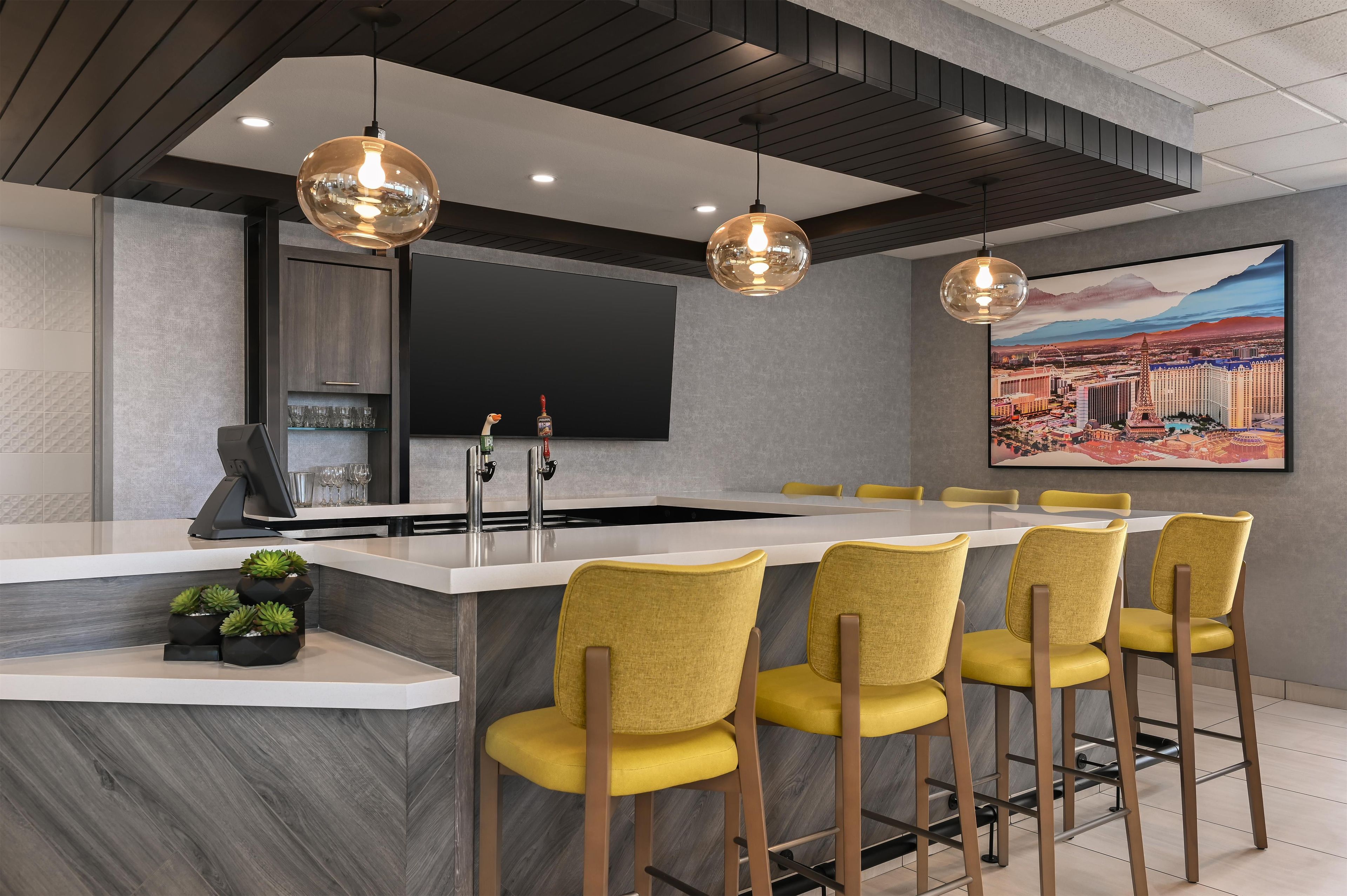 A modern kitchen with a central island, bar stools, a flat-screen TV, and a cityscape painting.