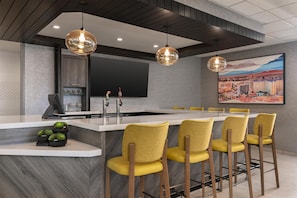 A modern kitchen with a central island, bar stools, a flat-screen TV, and a cityscape painting.
