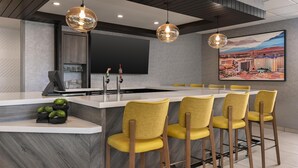 Een moderne keuken met een centraal eiland, barstoelen, hanglampen, een flatscreen televisie en een groot stadsgezicht schilderij.