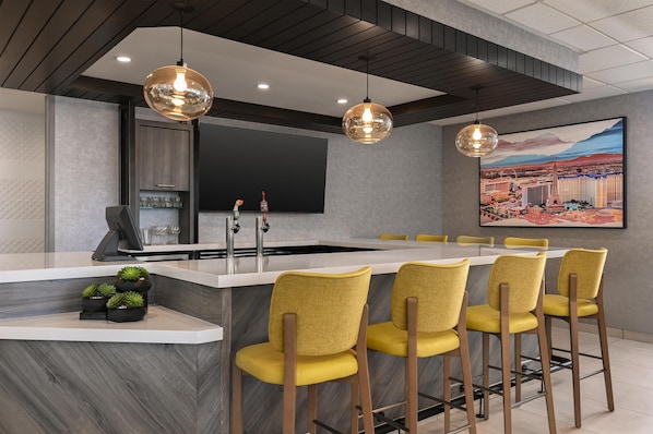 A modern kitchen with a central island, bar stools, pendant lighting, a flat-screen TV, and a large cityscape painting.