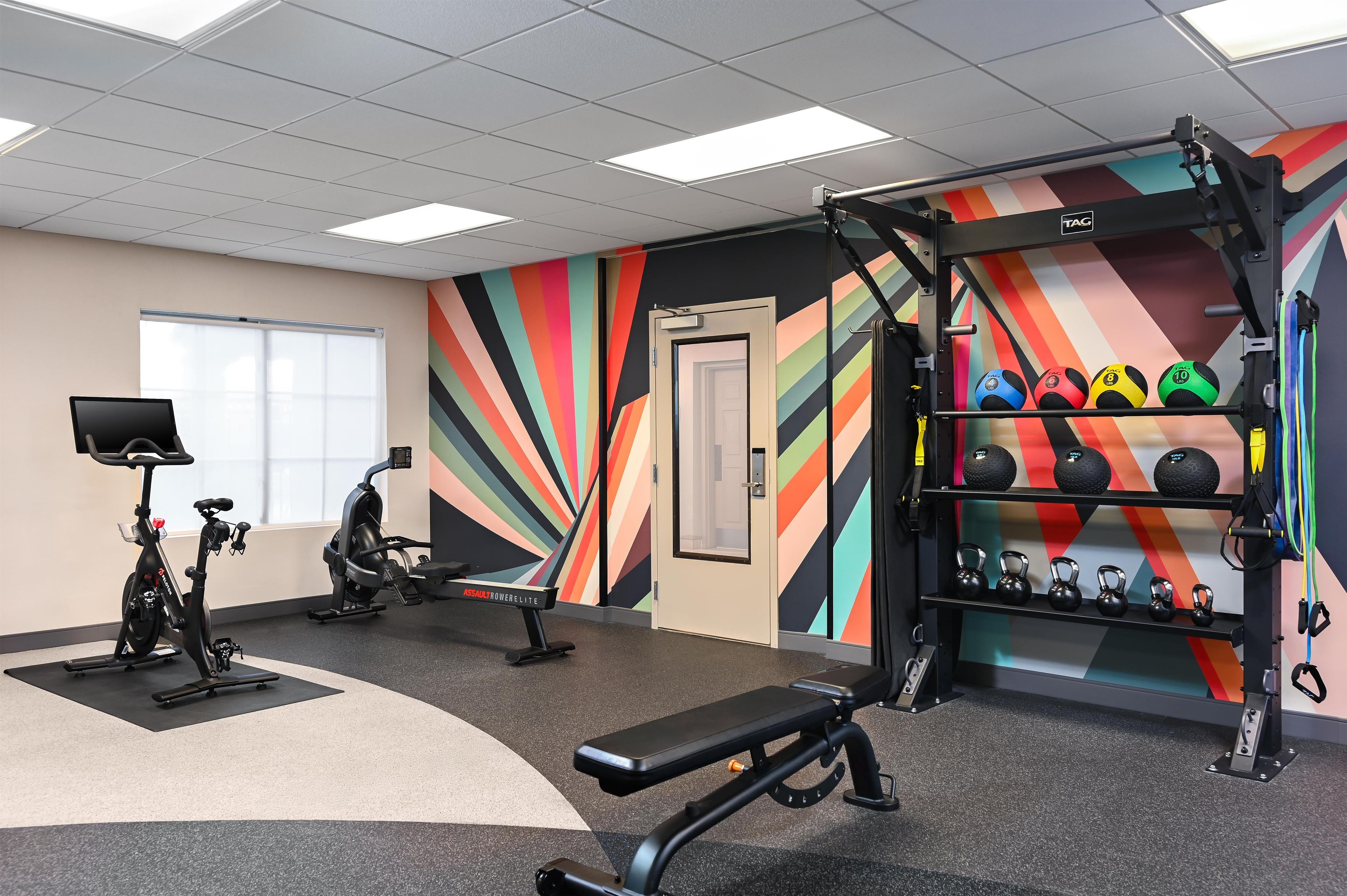 Un gimnasio con equipamiento de ejercicio, una pared con rayas de colores y una puerta.