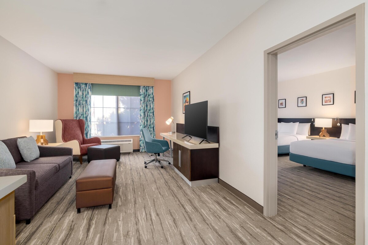 Habitación de hotel con sofá, sillón, escritorio, televisor y cama.