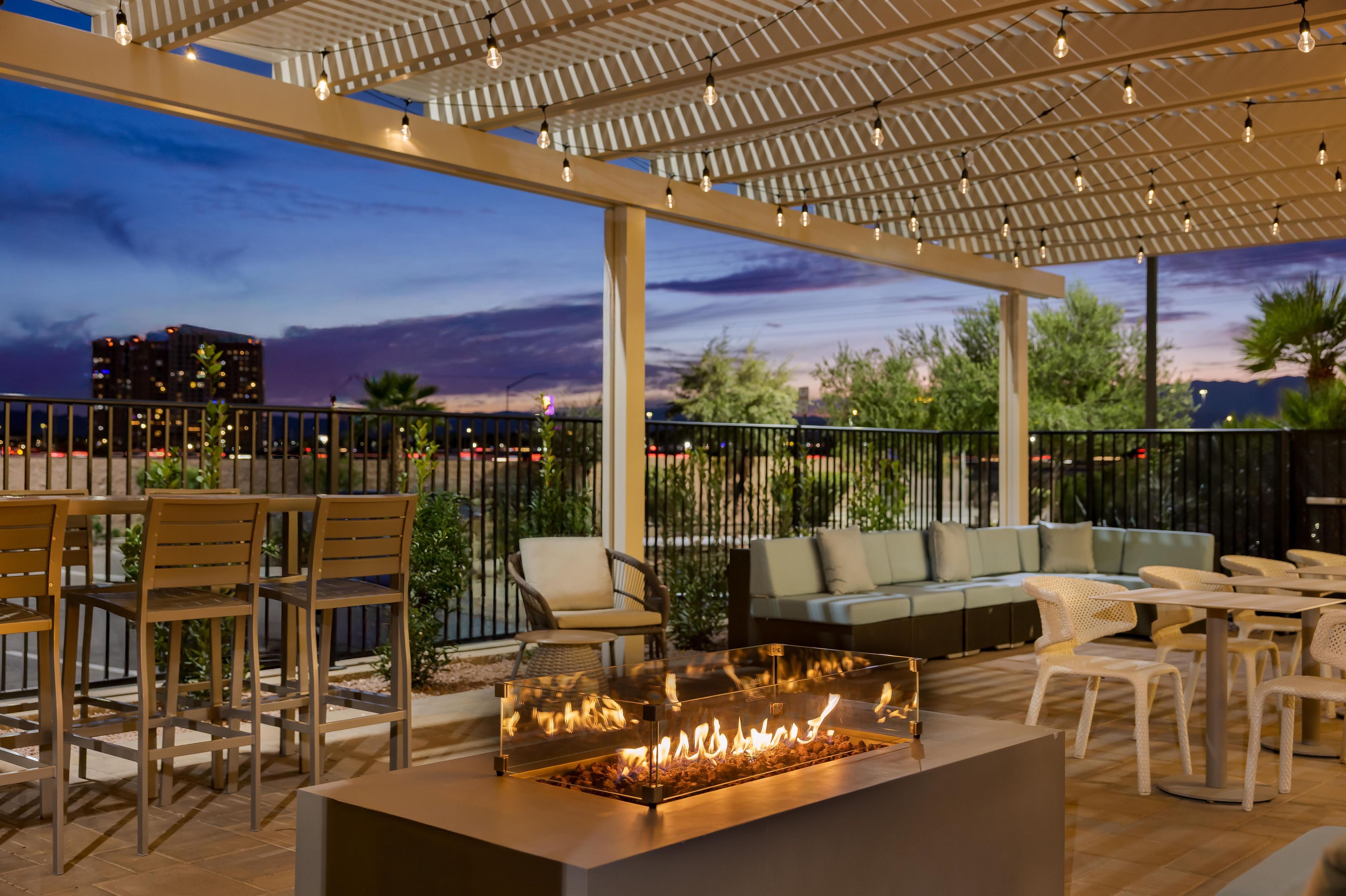 An outdoor patio area with a fire feature, seating, and a view of the cityscape at dusk.