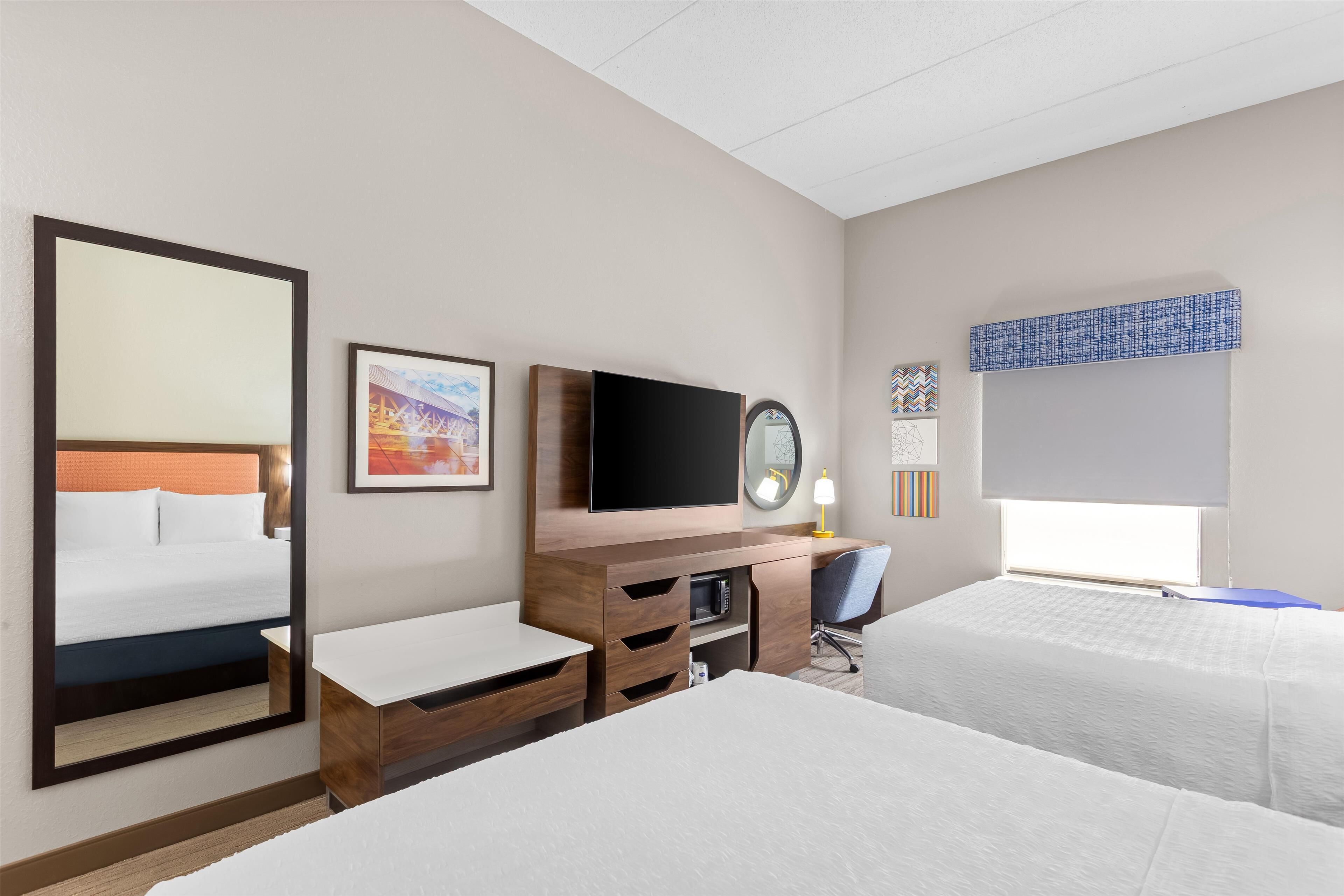 A hotel room with a large bed, a desk with a chair, a television, and a window with a view.