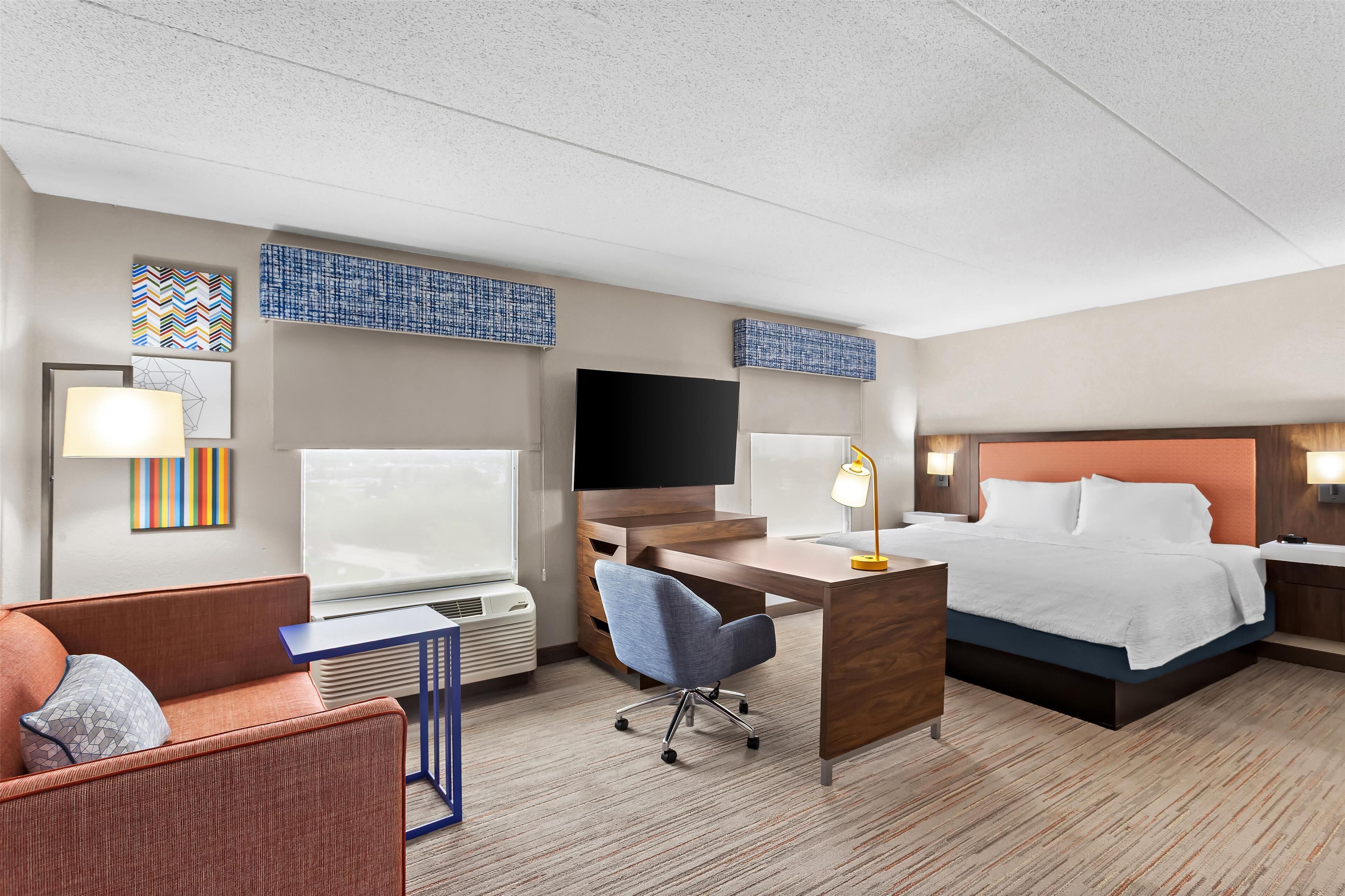 A hotel room with a bed, desk, chair, TV, and artwork on the walls.