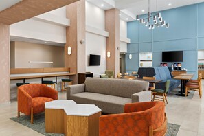 A modern lobby with seating areas, a reception desk, and a television screen.