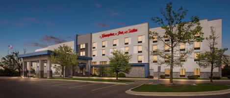 A Hampton Inn & Suites hotel with a modern design, featuring a large parking lot and a well-lit entrance.