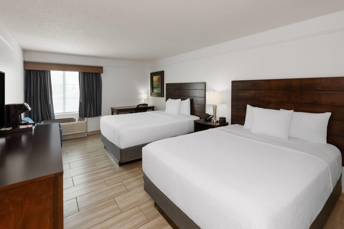 A hotel room with two beds, a desk, a chair, a lamp, and a painting on the wall.