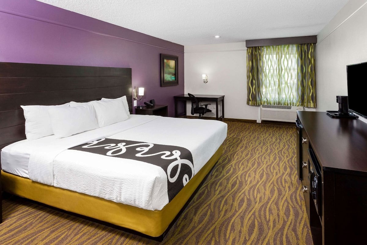 A hotel room with a large bed, a desk, a chair, a television, and a window with curtains.