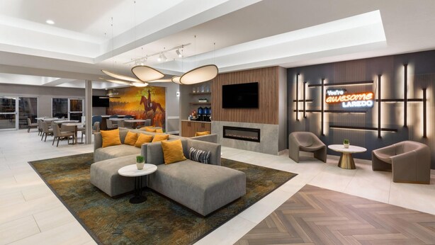 A modern interior with a sectional sofa, a fireplace, a TV, and a dining area. - La Quinta Inn & Suites by Wyndham Laredo Airport (Laredo)
