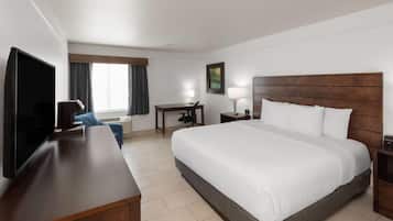 Une chambre d’hôtel avec un grand lit, un bureau, une chaise, une télévision et une fenêtre avec des rideaux.