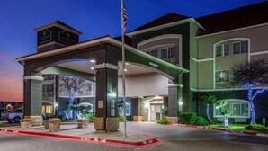 A hotel entrance with a covered walkway, American flag, and illuminated trees. - La Quinta Inn & Suites by Wyndham Laredo Airport (Laredo)