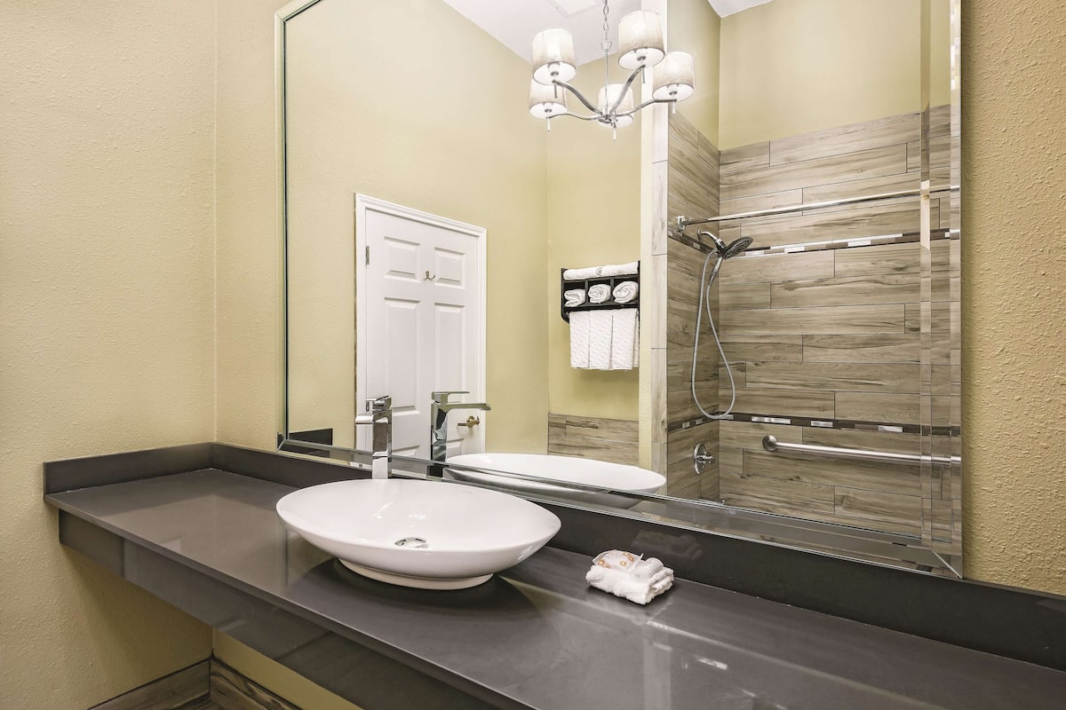 A bathroom with a large mirror, a vessel sink, a towel rack, and a shower with a wooden panel design.