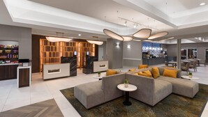 A modern hotel lobby with a reception desk, a bar area, and a seating area with a sectional sofa and a small round table. - La Quinta Inn & Suites by Wyndham Laredo Airport (Laredo)