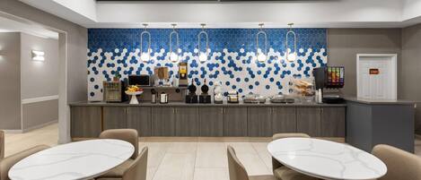 A modern hotel lobby with a central counter, seating area, and a decorative wall.