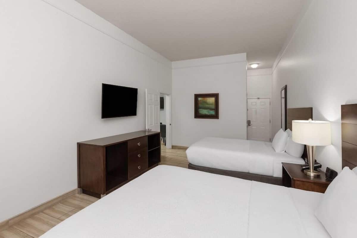A hotel room with two beds, a TV, a painting, and a bedside lamp.