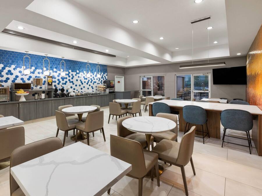 A modern restaurant with round tables and chairs, a counter with a blue and white patterned wall, and a large painting on the right.