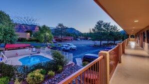 A hotel balcony with a pool, a parking lot, and a mountain view.