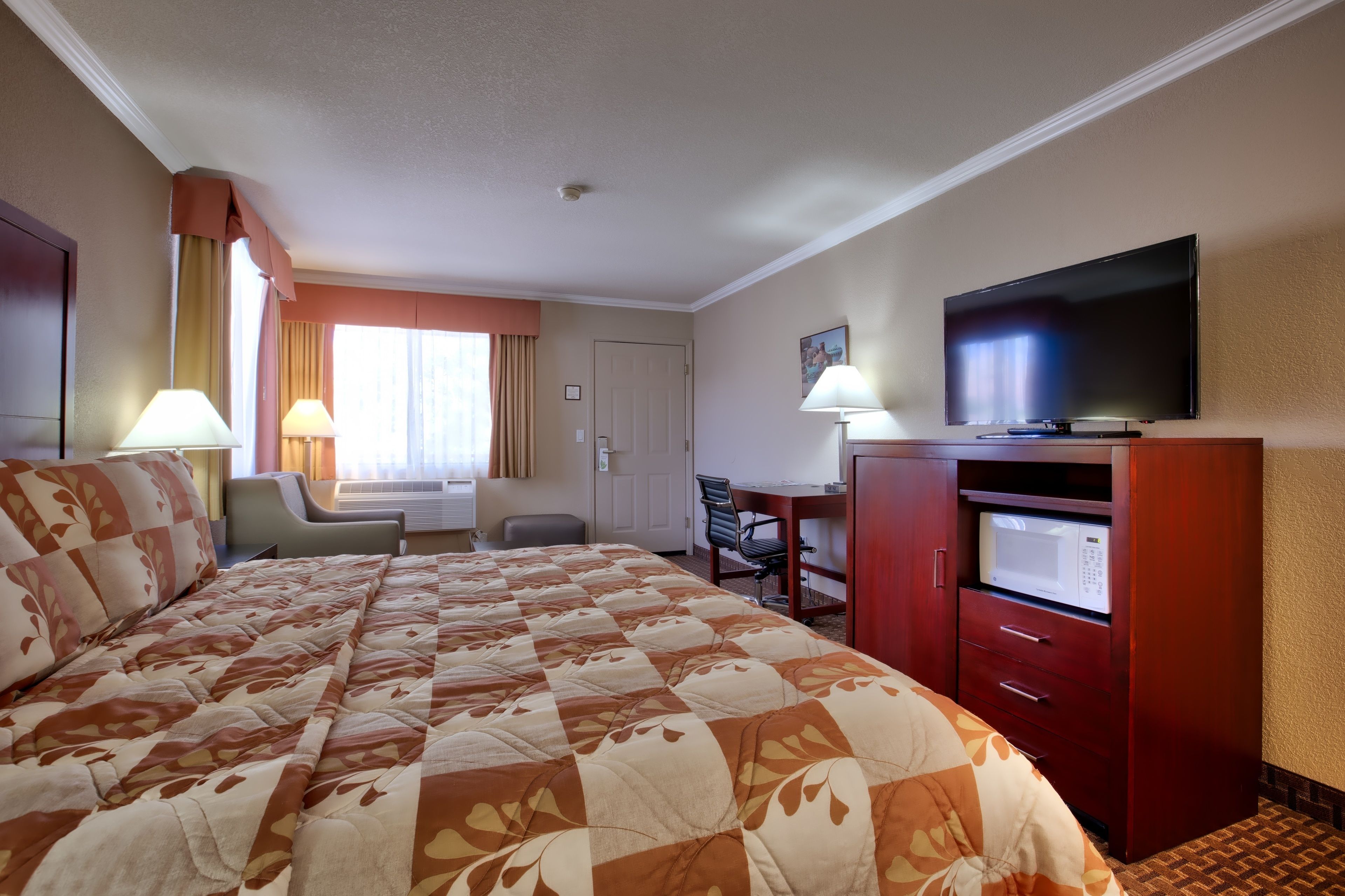 Une chambre d’hôtel avec un grand lit, une télévision, un bureau avec une chaise et un four à micro-ondes.