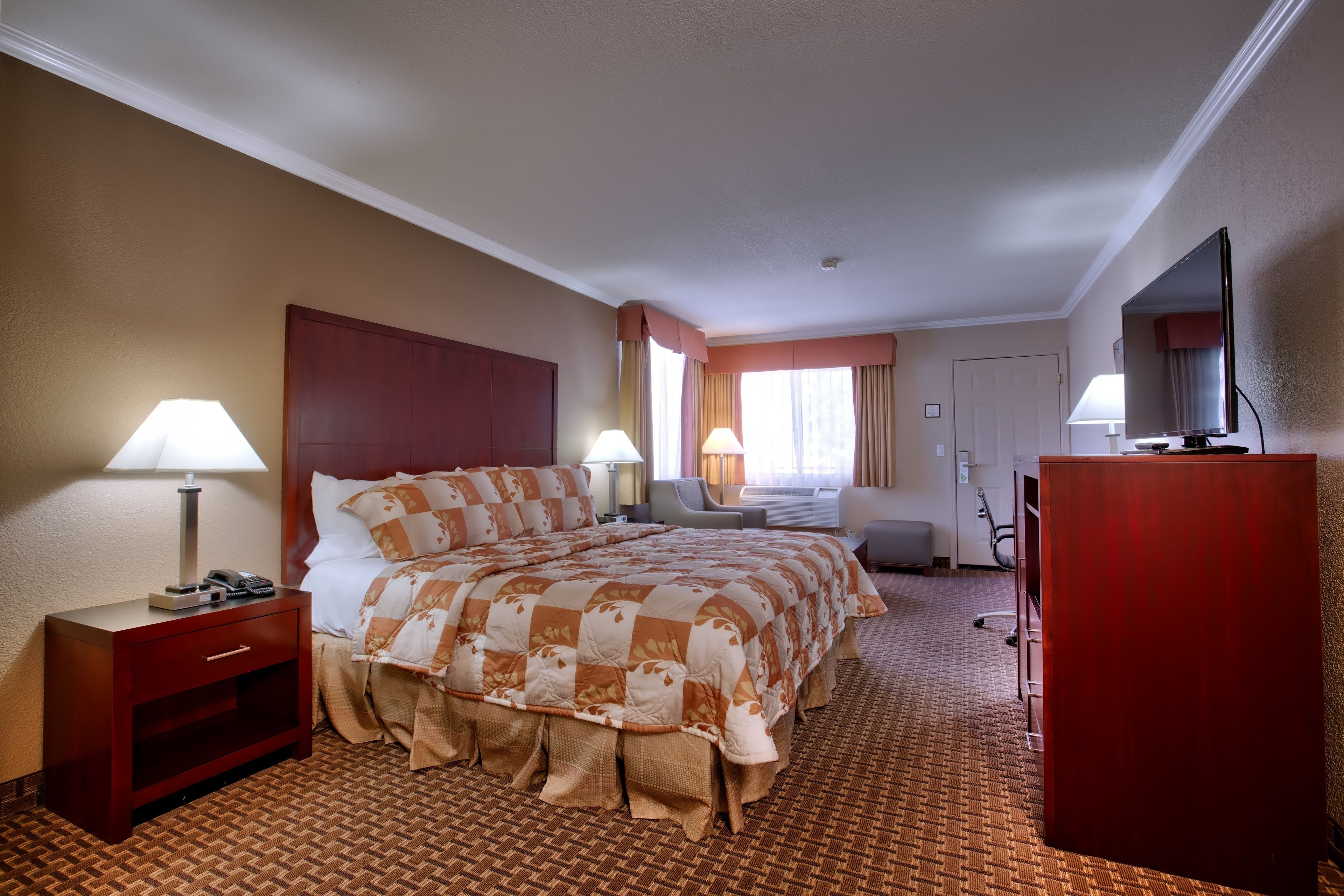 A hotel room with a large bed, two bedside tables, a desk, a television, and a window with curtains.