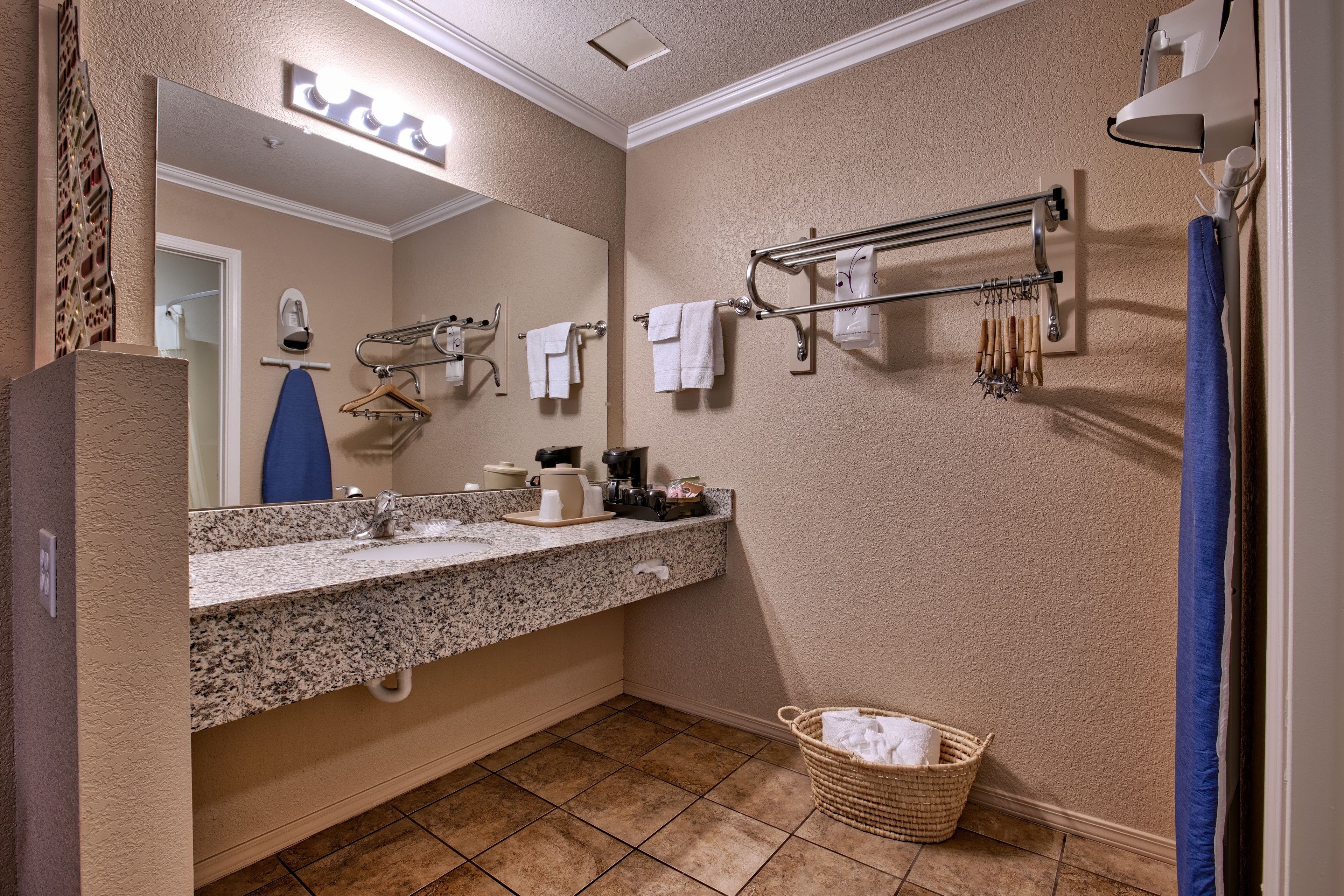 Un baño con lavamanos de granito, un espejo, toalleros y una cesta.