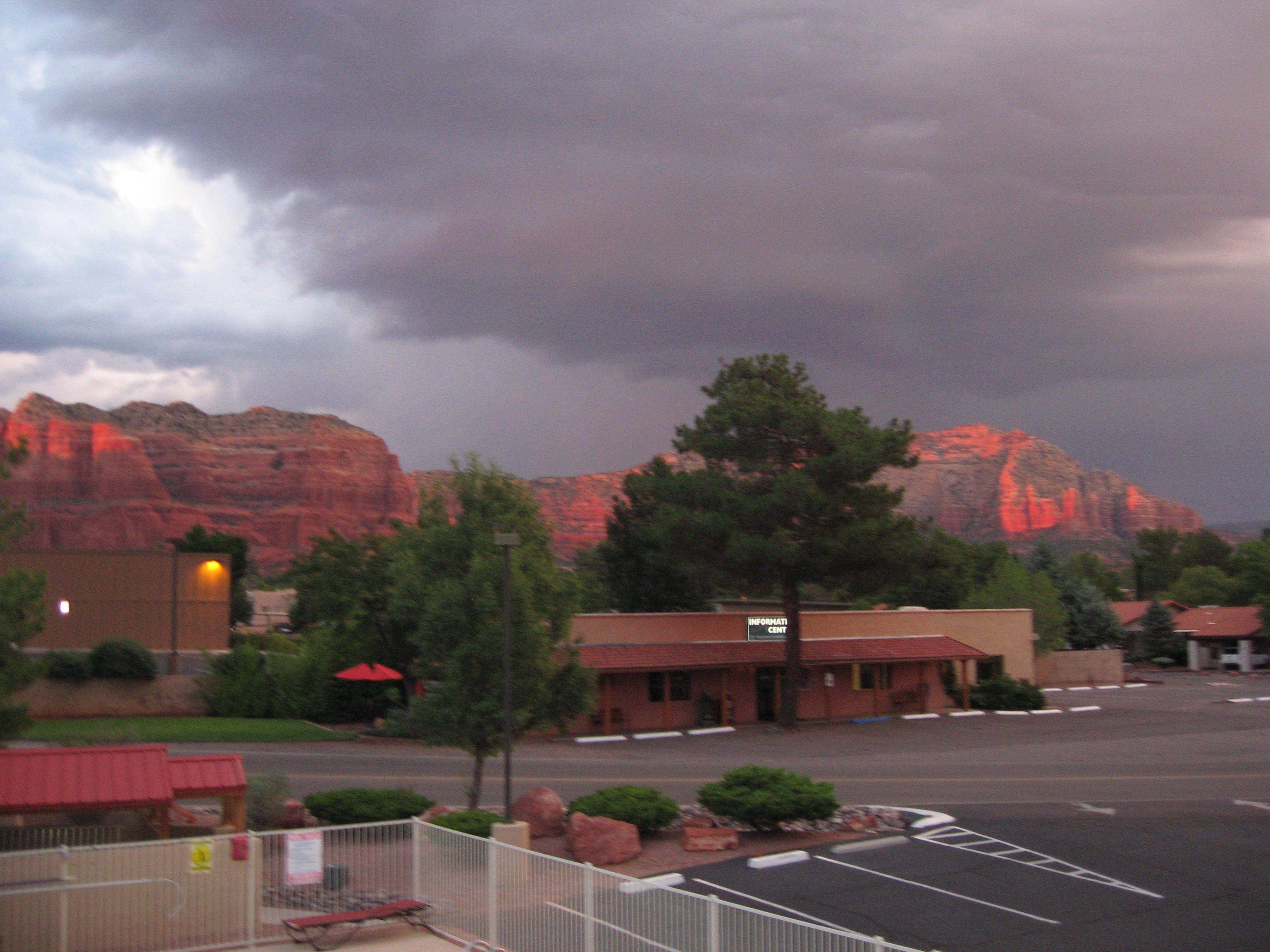 A parking lot with a building labeled "INFORMATION CENTRE" in the foreground, surrounded by trees and a mountainous backdrop.