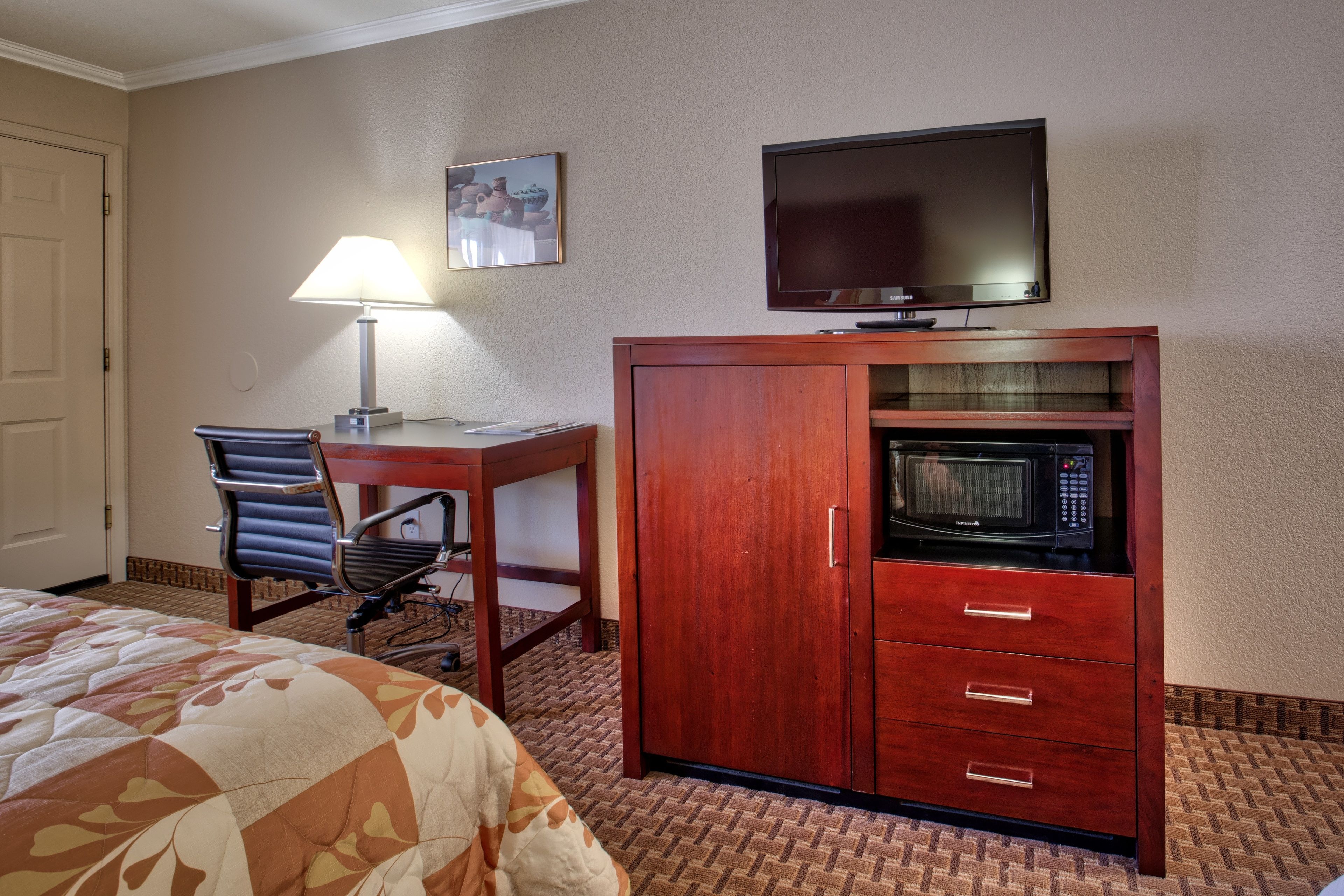 A hotel room with a bed, a desk with a lamp, a television, and a microwave.