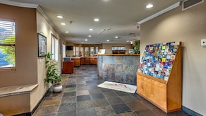 A hotel lobby with a reception desk, a display of postcards, and a tiled floor.