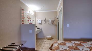 A compact hotel room with a bed, a small bathroom with a sink and towel rack, and a laundry basket.