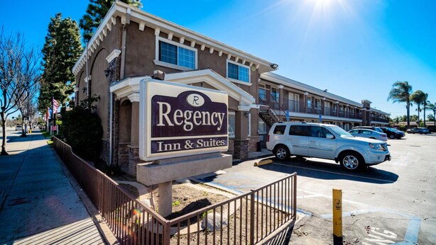 Un bâtiment de la chaîne Regency Inn & Suites, avec une enseigne, un parking et un ciel bleu dégagé.