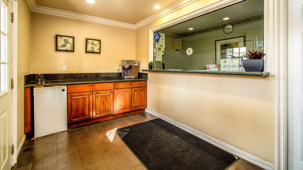 A kitchen with wooden cabinets, a refrigerator, a coffee maker, and a window with a view. - Regency Inn & Suites (Downey)